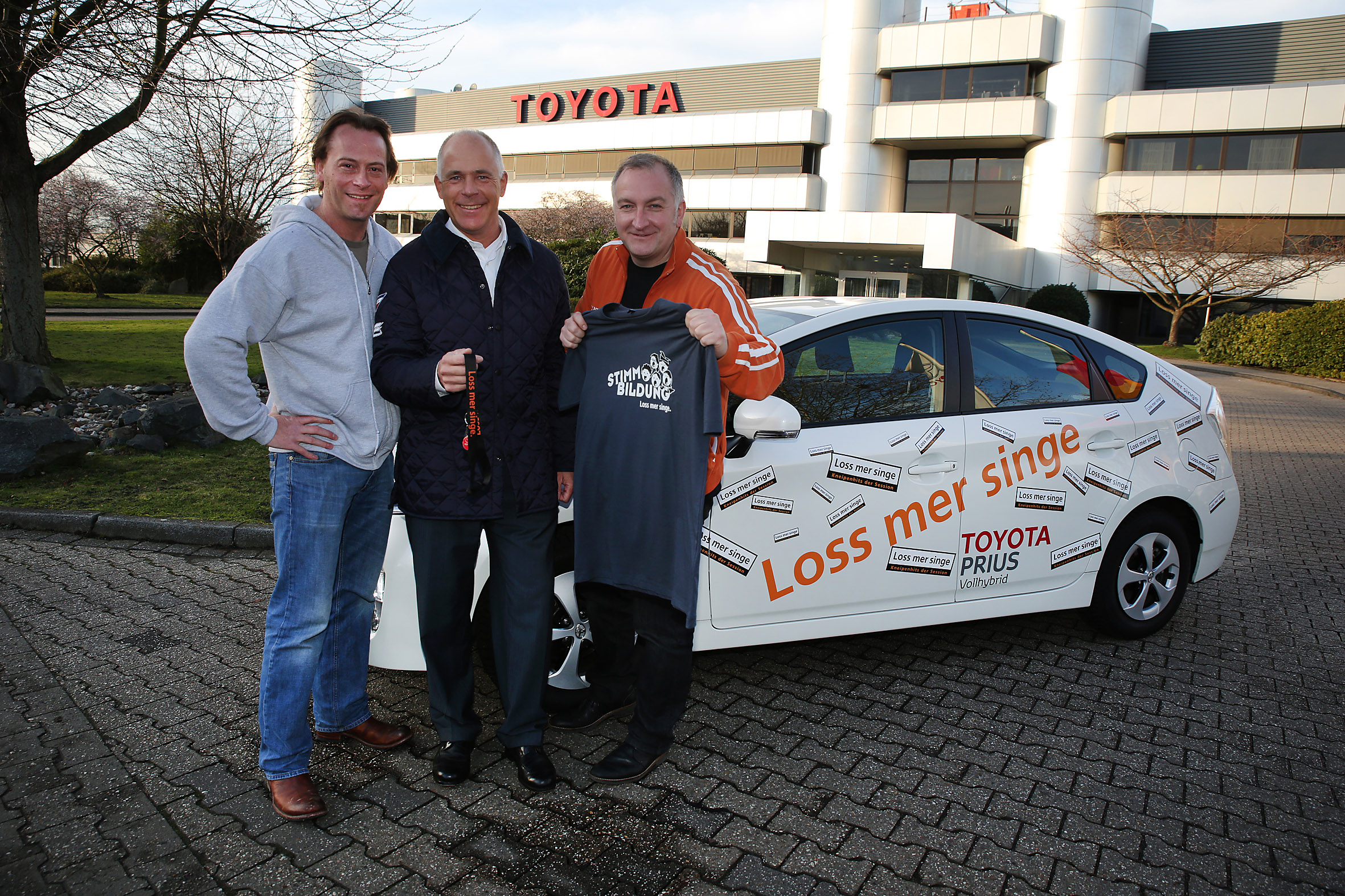 Ekkardt Sensendorf, Toyota Deutschland (Mitte), übergibt einen Toyota Prius als Tourfahrzeug an Georg Hinz, Vorstandsmitglied und Armin Schäfer (beide "Loss mer singe")
